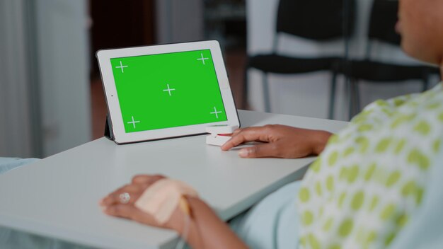 Gros plan d'un écran vert horizontal sur une tablette numérique en salle d'hôpital. Patient malade regardant un arrière-plan isolé et un modèle de maquette avec clé chroma sur l'affichage du gadget. La technologie