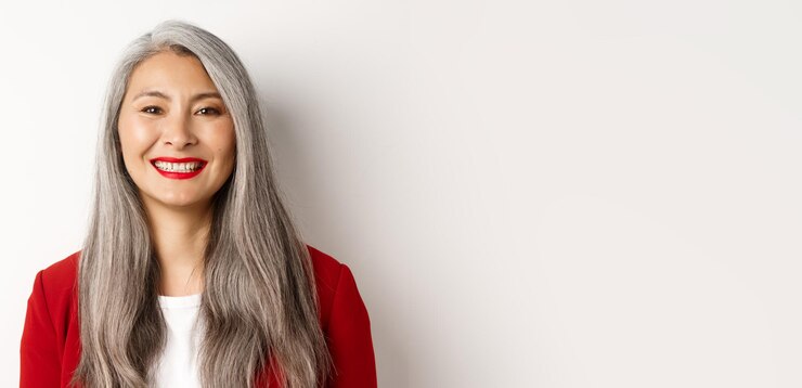 Photo gratuit gros plan d'une élégante femme mature en blazer rouge et maquillage souriant heureux à la caméra debout sur blanc