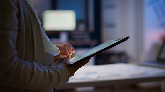 Gros plan sur une employée qui envoie des SMS, envoie et lit des messages pendant la pause, debout dans un bureau d'affaires tard dans la nuit. Femme d'affaires utilisant le surmenage sans fil du réseau de technologie moderne à minuit