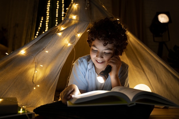 Gros plan sur un enfant lisant dans sa tente de maison