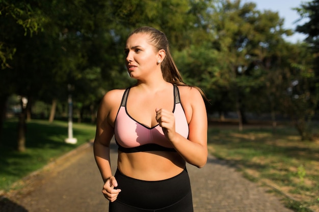 Gros plan épuisé femme de taille plus en haut sportif et leggings regardant fatigué de côté tout en courant dans le parc de la ville