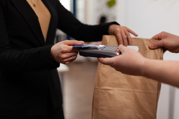 Gros plan d'une femme d'affaires détenant une carte de crédit de pos, utilisant la technologie sans contact, payant des plats à emporter du courrier