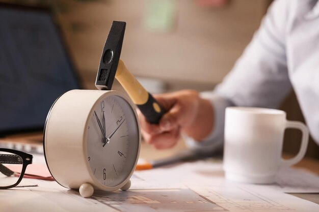 Gros plan d'une femme d'affaires frappant l'horloge sur son bureau tout en travaillant au bureau