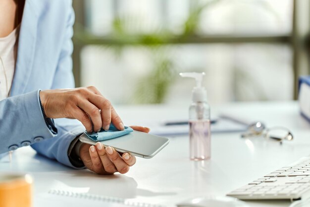 Gros plan d'une femme d'affaires utilisant un chiffon et nettoyant son téléphone portable au bureau