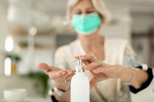 Gros plan d'une femme âgée utilisant un désinfectant pour les mains à la maison