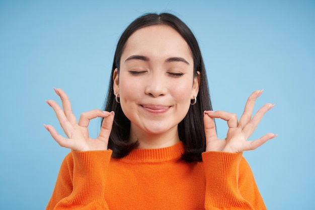 Gros plan d'une femme asiatique souriante et satisfaite montre un signe correct ok avec un visage heureux se dresse sur le dos bleu
