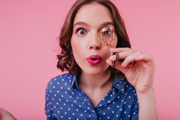 Gros plan d'une femme aux yeux bruns avec une expression de visage surpris recourbe ses cils. adorable fille caucasienne aux cheveux courts se préparant pour la date.