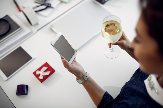 Photo gratuite gros plan d'une femme buvant du vin et utilisant un téléphone intelligent au bureau