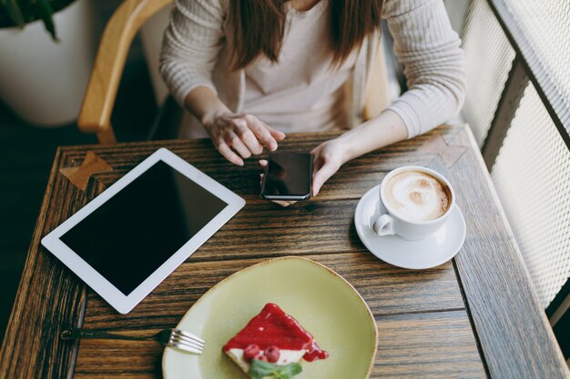 Gros plan femme dans un café avec tablette ordinateur tasse de gâteau cappuccino se détendre au restaurant pendant le temps libre. femme tenant un téléphone portable avec un écran vide vierge reste au café. concept de mode de vie.