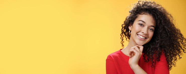 Photo gratuit gros plan d'une femme élégante et heureuse aux cheveux bouclés brillants en robe rouge inclinant la tête sensuellement touc