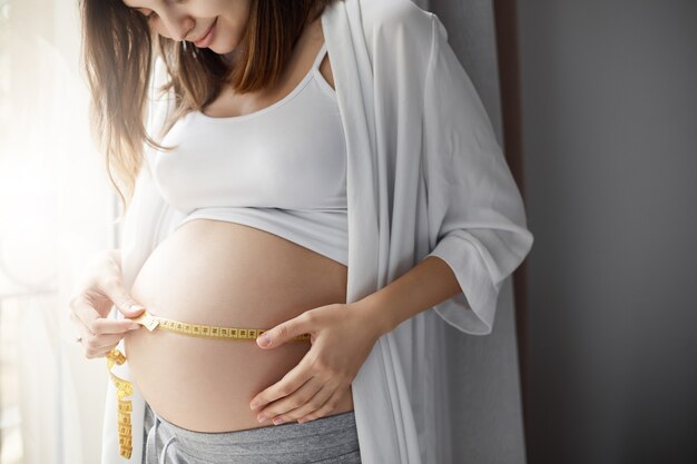 Gros plan d'une femme enceinte mesurant son ventre pour suivre le développement de son enfant. Heureuse mère soucieuse d'une grossesse en bonne santé.