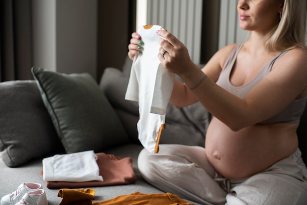 Gros plan femme enceinte regardant les vêtements de bébé