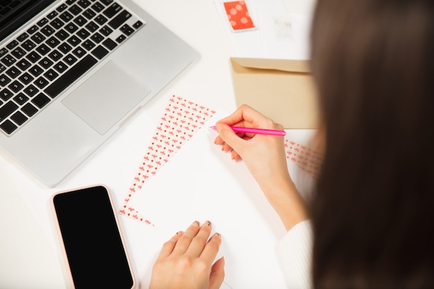 Gros plan femme faisant carte de voeux pour le nouvel an et Noël 2021 pour les amis ou la famille, réservation de ferraille, bricolage. Rédigez une lettre avec les meilleurs vœux, concevez sa carte maison. Vacances, fête.