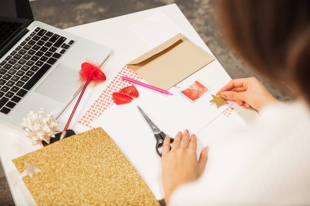 Gros plan femme faisant carte de voeux pour le nouvel an et Noël 2021 pour les amis ou la famille, réservation de ferraille, bricolage. Rédigez une lettre avec les meilleurs vœux, concevez sa carte maison. Vacances, fête.