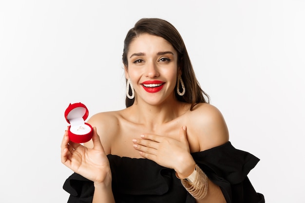 Gros plan d'une femme heureuse montrant sa bague de fiançailles, recevoir une demande en mariage, en disant oui, debout sur fond blanc.