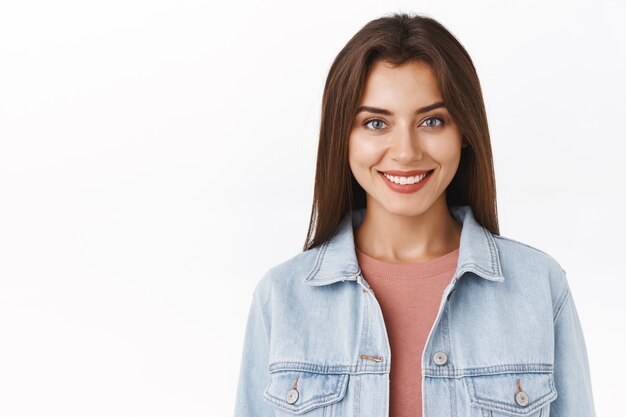 Gros plan, femme heureuse séduisante, confiante et affirmée en veste en jean, t-shirt, souriante déterminée avec une expression satisfaite et sûre d'elle, exprimer son enthousiasme et sa joie, se tenir sur fond blanc