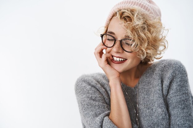 Gros plan d'une femme hipster sensuelle et tendre en bonnet et pull d'hiver fermer les yeux en inclinant la tête et souriante, coquette, touchante la joue tendre et douce, rappelant de beaux souvenirs chaleureux