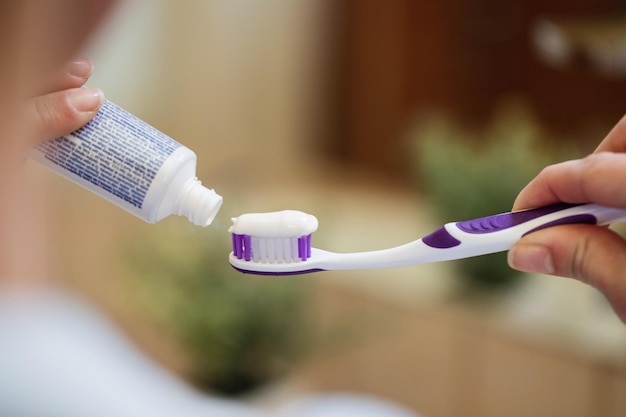 Gros plan d'une femme méconnaissable appliquant du dentifrice sur une brosse à dents dans la salle de bain