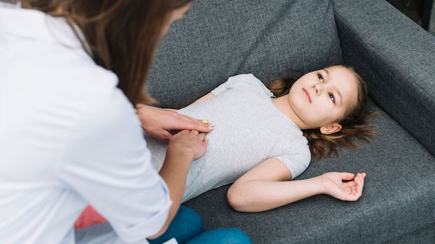 Gros plan, de, femme médecin, examiner, patient fille, mensonge, sur, gris, sofa