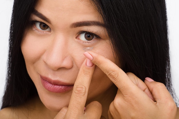 Gros plan d'une femme mettant des lentilles de contact sur fond blanc. Dame mettant des lentilles et regardant la caméra.