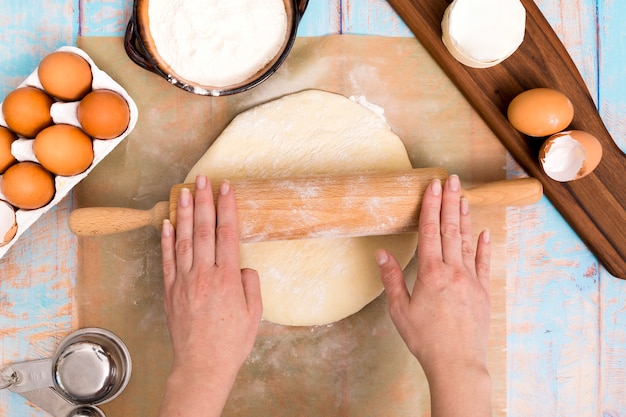 Gros plan, femme, rouler, pâte, rouleau à pâtisserie, ingrédients, bureau, bois