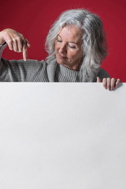 Gros plan d&#39;une femme senior pointant sur un panneau blanc noir sur la surface rouge