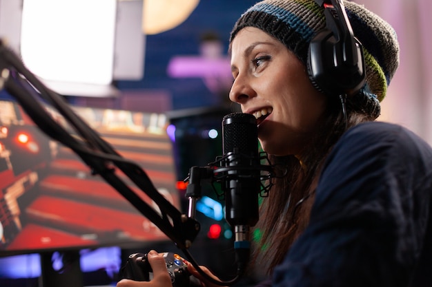 Gros plan d'une femme streamer parlant dans un microphone professionnel en home studio. Tournoi de jeu en ligne en streaming en ligne à l'aide d'un réseau technologique sans fil