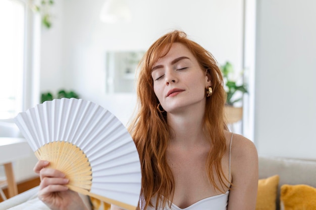 Gros plan femme surchauffée agitant un ventilateur en papier respirant de l'air penché en arrière sur un canapé seul souffrant de fièvre de chauffage ou d'un temps chaud d'été à la maison