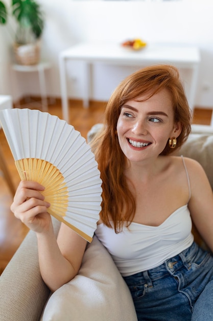 Gros plan femme surchauffée agitant un ventilateur en papier respirant de l'air penché en arrière sur un canapé seul souffrant de fièvre de chauffage ou d'un temps chaud d'été à la maison