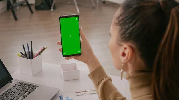 Gros plan d'une femme tenant verticalement un écran vert sur un smartphone. téléphone portable avec affichage chroma ky, arrière-plan isolé et modèle de maquette. téléphone portable avec chroma-key et maquette.
