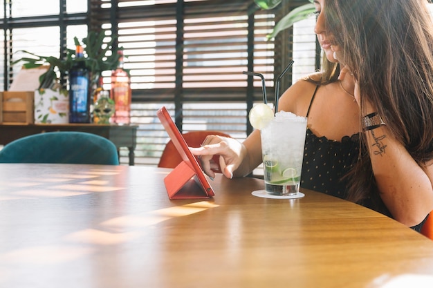 Gros plan, femme, toucher, tablette numérique, à, verre cocktail, sur, table en bois