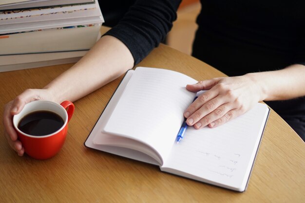 Gros plan d'une femme travaillant ou étudiant à domicile avec un café rouge à la main