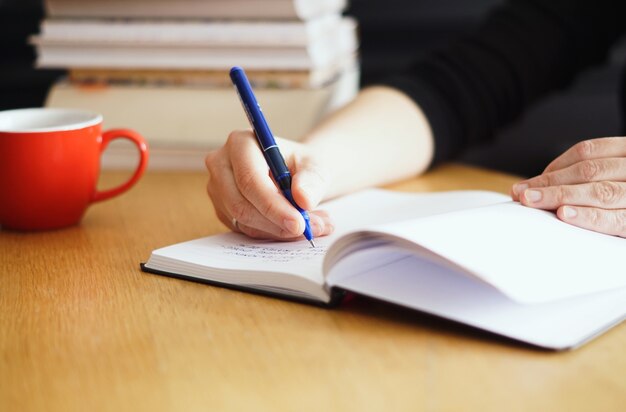 Gros plan d'une femme travaillant ou étudiant à domicile avec une tasse de café rouge à proximité