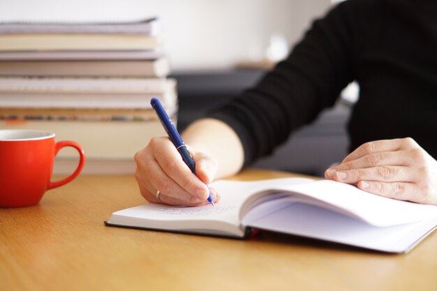 Gros plan d'une femme travaillant ou étudiant à domicile avec une tasse de café rouge à proximité