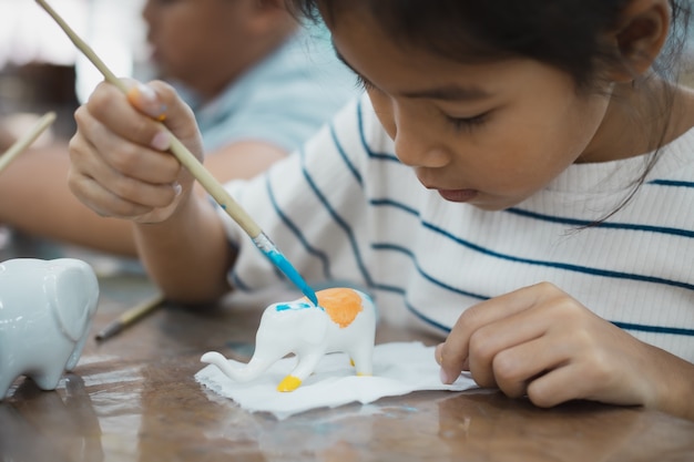 Gros plan fille enfant asiatique se concentre pour peindre sur un petit éléphant en céramique avec de la couleur à l'huile. classe d'activités créatives d'arts et d'artisanat pour enfants à l'école.