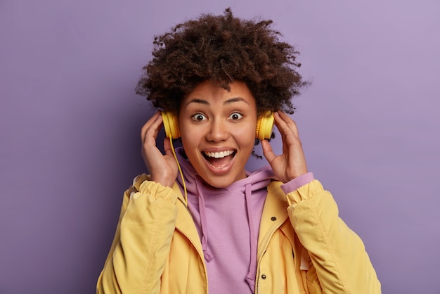 Gros plan d'une fille hipster joyeuse émotive porte des écouteurs, aime le rythme de la musique, écoute la piste audio, a une expression insouciante