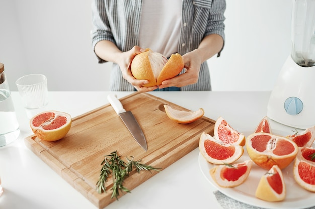 Gros plan de fille peler le pamplemousse sur le mur blanc. Concept de nutrition de remise en forme saine.