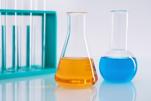 Gros plan d'une fiole Erlenmeyer avec un liquide orange et une fiole ronde avec un liquide bleu dans un laboratoire