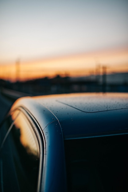 Gros plan de gouttes de pluie sur un toit de voiture avec le ciel coucher de soleil se reflétant dans les fenêtres