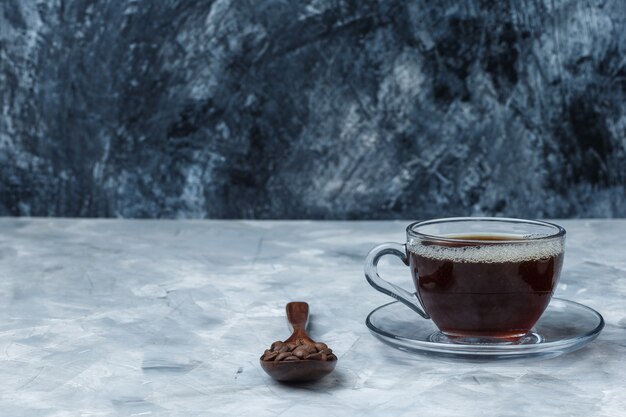 Gros plan de grains de café dans une cuillère en bois avec une tasse de café