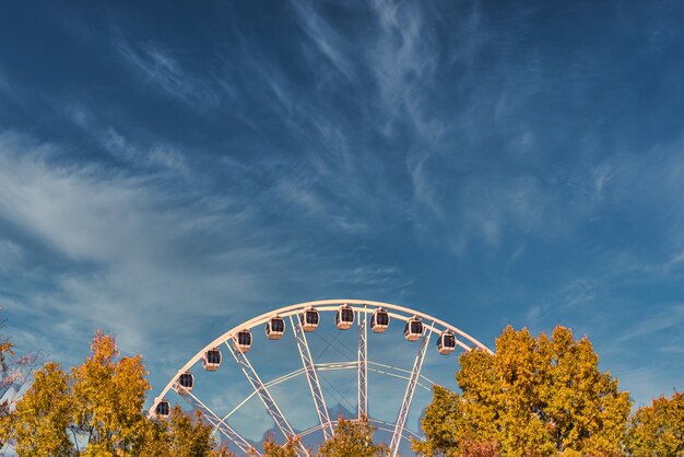 Gros plan d'une grande roue près des arbres sous un ciel bleu nuageux