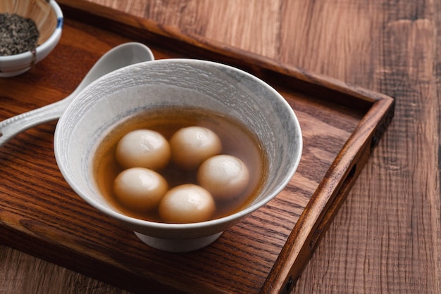 Gros plan sur un gros tangyuan au sésame (tang yuan, boulettes de riz gluant) avec une soupe au sirop sucré dans un bol sur fond de table en bois pour la nourriture du festival du solstice d'hiver.