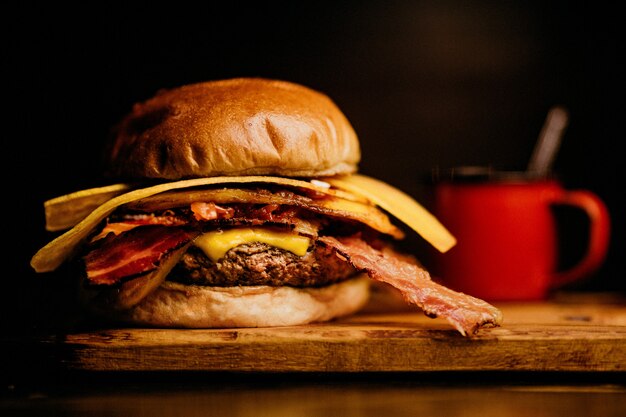 Gros plan d'un hamburger avec du bacon et du fromage, une tasse de café rouge