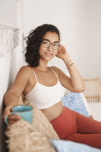 Gros plan heureux jeune femme en bonne santé avec des cheveux bouclés sombres couché dans un canapé confortable dans une terrasse