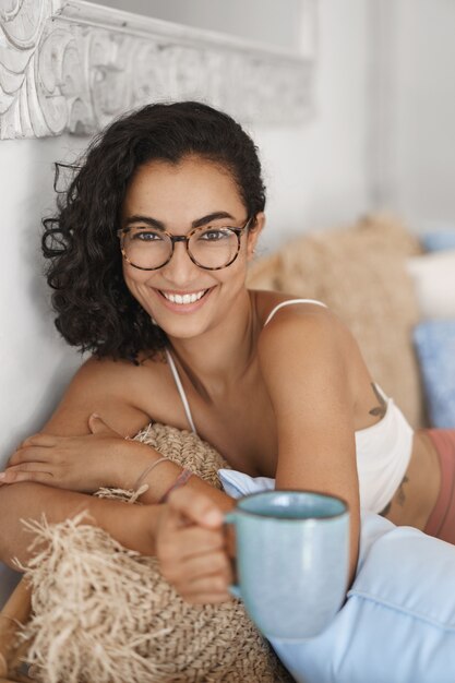 Gros plan heureux jeune femme en bonne santé avec des cheveux bouclés sombres couché dans un canapé confortable dans une terrasse