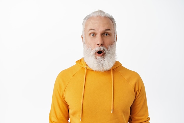 Photo gratuite gros plan d'un hipster senior impressionné haletant en disant wow vieil homme barbu laisse tomber la mâchoire et regarde avec admiration la caméra en train de vérifier une publicité géniale gros accord promotionnel fond blanc