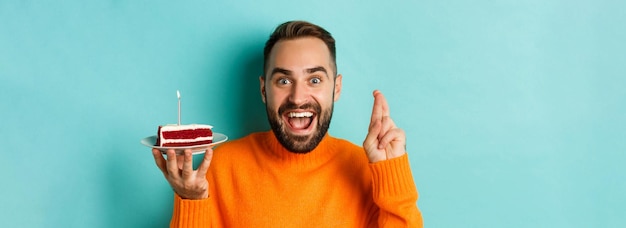 Gros plan d'un homme adulte heureux célébrant son anniversaire tenant un gâteau d'anniversaire avec une bougie et faisant un vœu standi