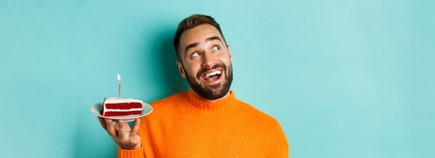 Photo gratuite gros plan d'un homme adulte heureux célébrant son anniversaire tenant un gâteau d'anniversaire avec une bougie et faisant un vœu standi