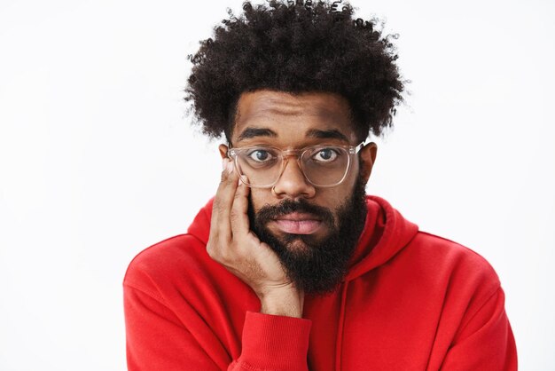 Gros plan d'un homme afro-américain contrarié solitaire et sombre avec une barbe et une coiffure afro dans des verres penché la tête sur la paume en soupirant et en ayant l'air malheureux