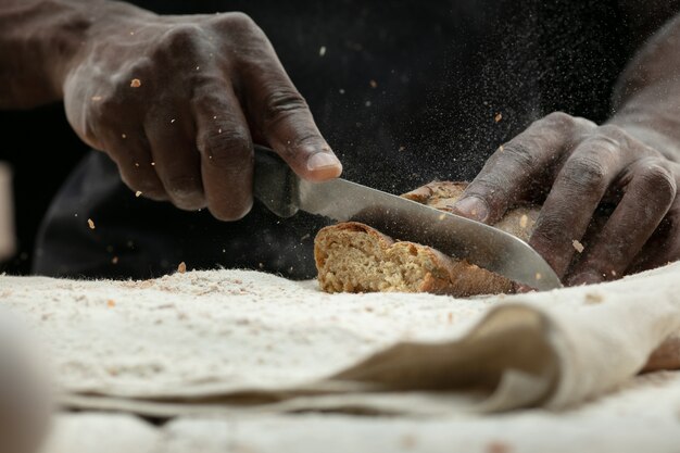 Gros plan de l'homme afro-américain tranches de pain frais avec un couteau de cuisine